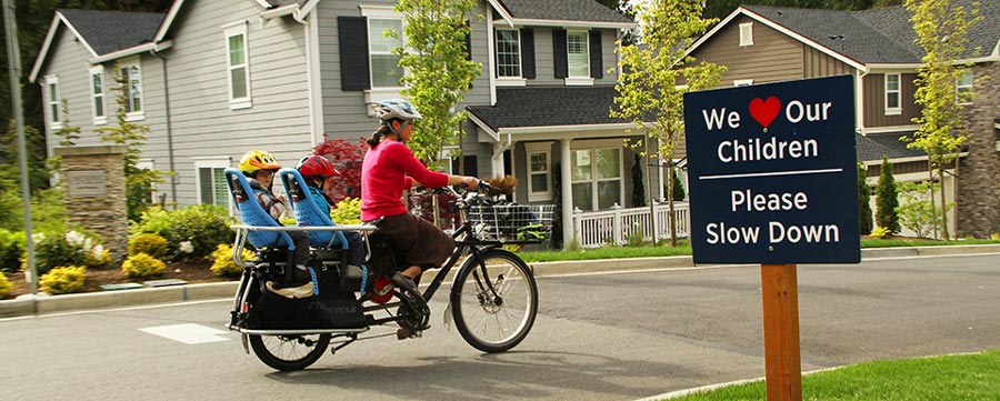 A woman with her children in seats on the back of her bicycle rides through a neighborhood.