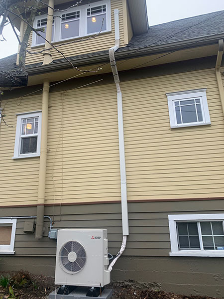 heat pump on yellow house with pipe connecting to upper level